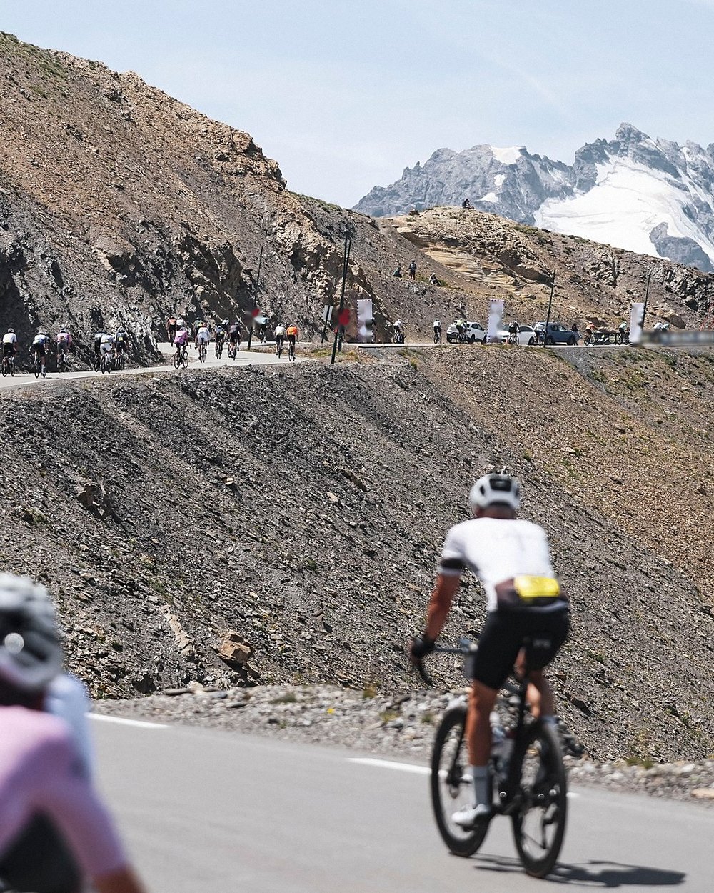 Un cycliste attaque les derniers lacets d'un col, sommets enneigés au fond