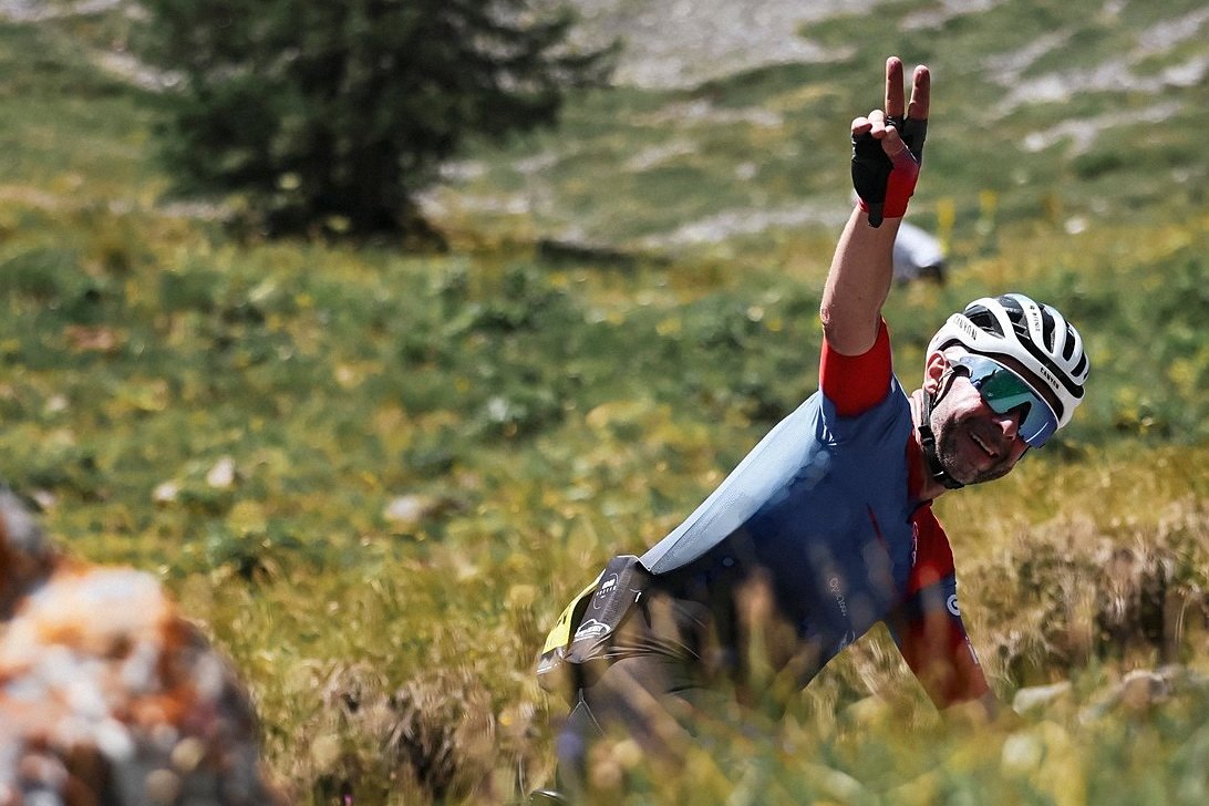 Un cycliste fait le V de la victoire au milieu d'un alpage fleuri